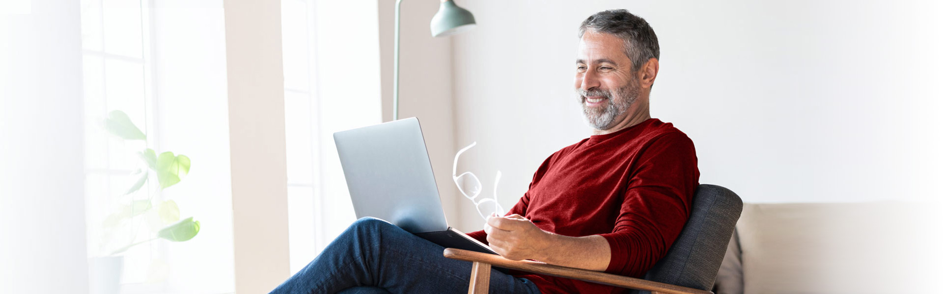 A man in a red sweater smiles down at his laptop.