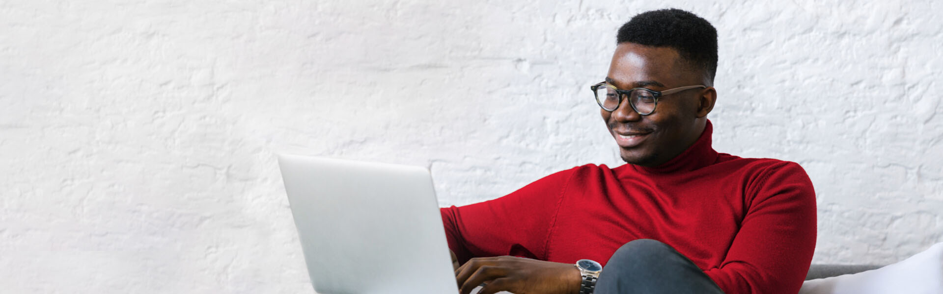 A well-dressed man sits at his computer while smiling.