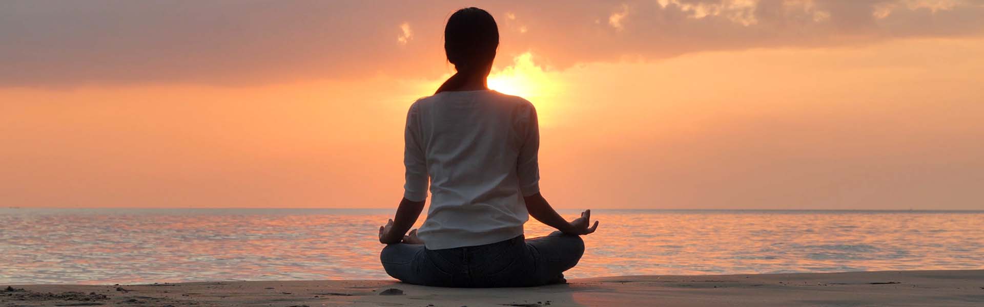 Person sitting in a yoga pose looking at a sunrise over the ocean.
