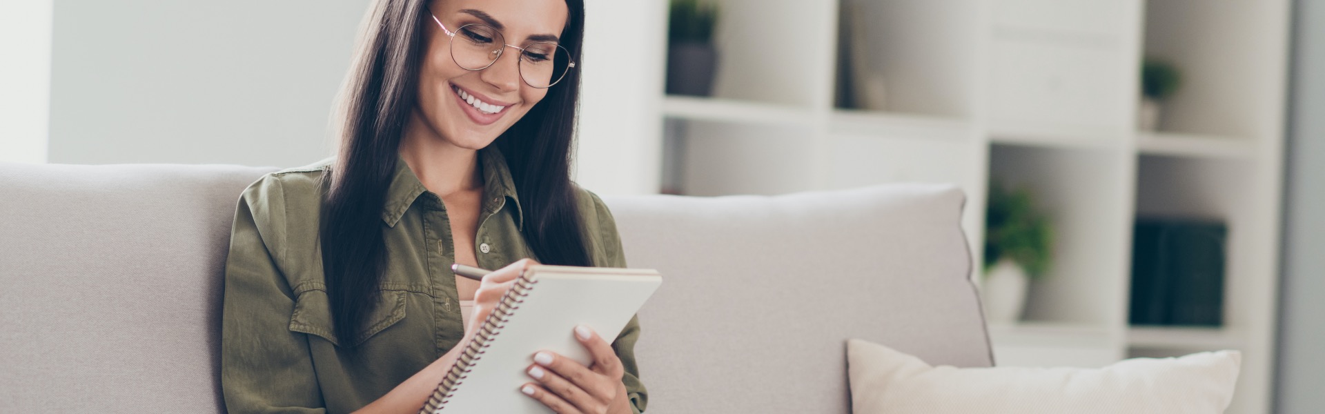 A woman sitting on a sofa smiles as she looks at information on her laptop.