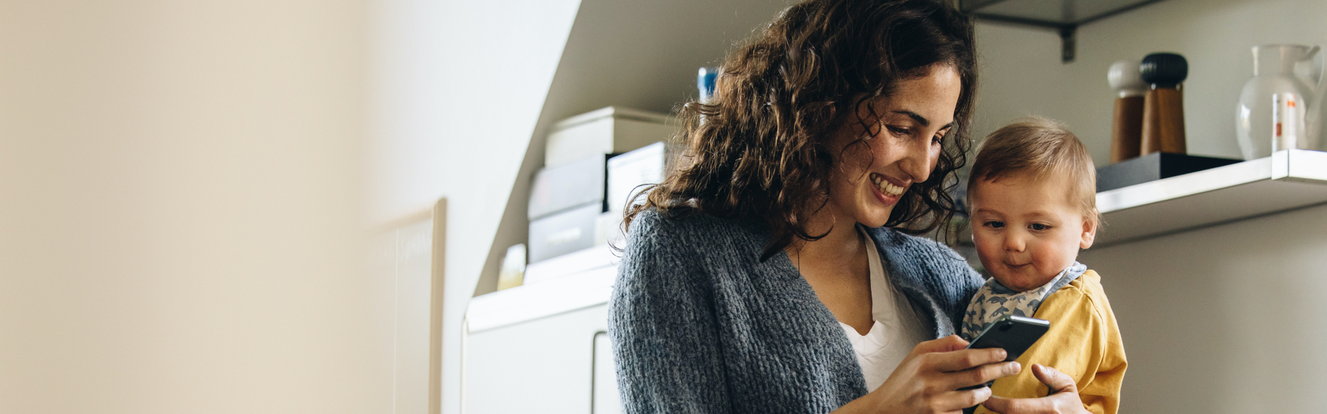 A mother and her child are smiling while looking at a smartphone.