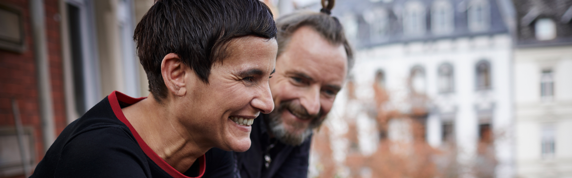 A middle-aged man and woman are smiling at the ground.