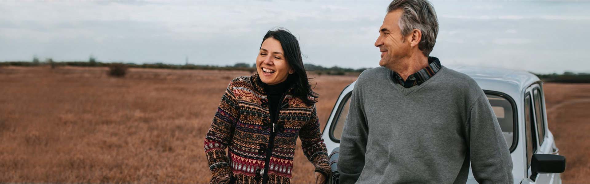 Relaxed, laughing couple with their car in a field.