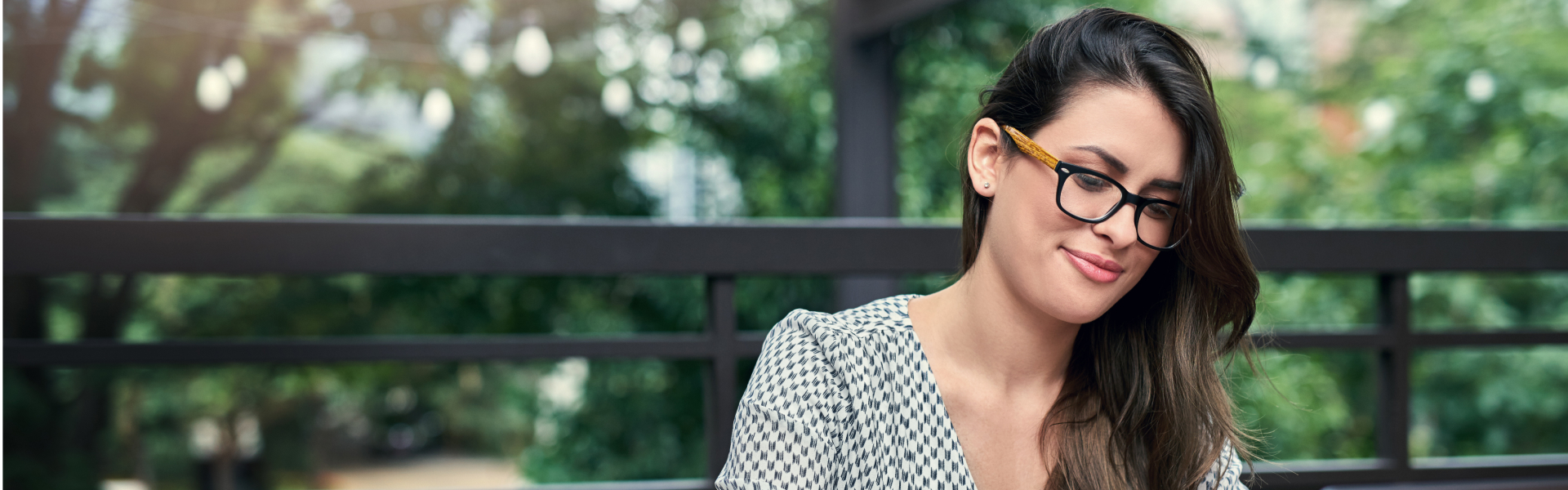 A woman sitting outside is looking down at something out of the frame.