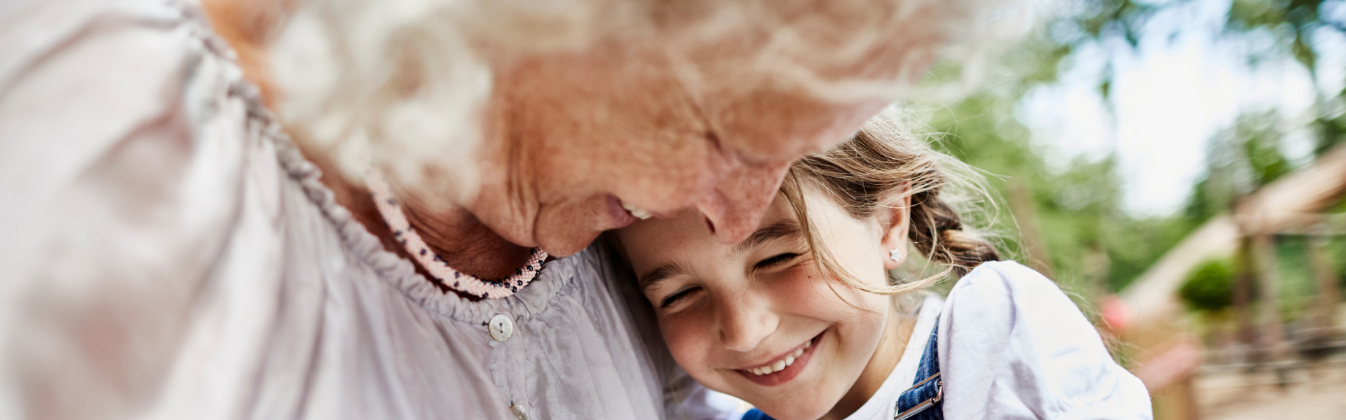 A young smiling girl is leaning into an older woman’s chest.