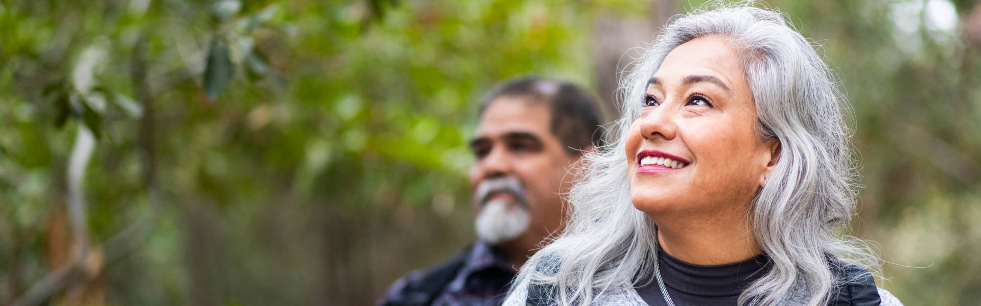 A woman smiles as she hikes in the woods with a man.