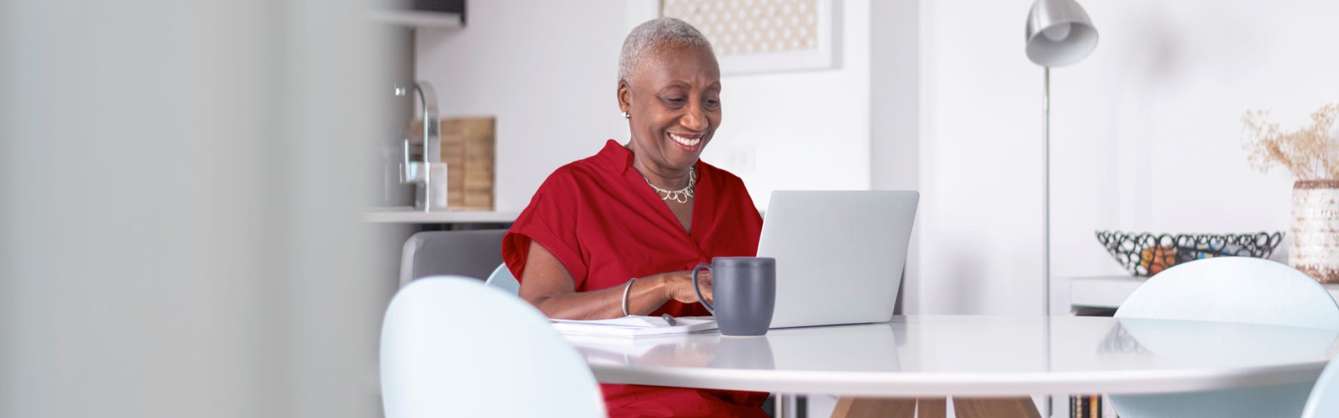 An older woman sitting at a table, typing on her laptop and smiling.
