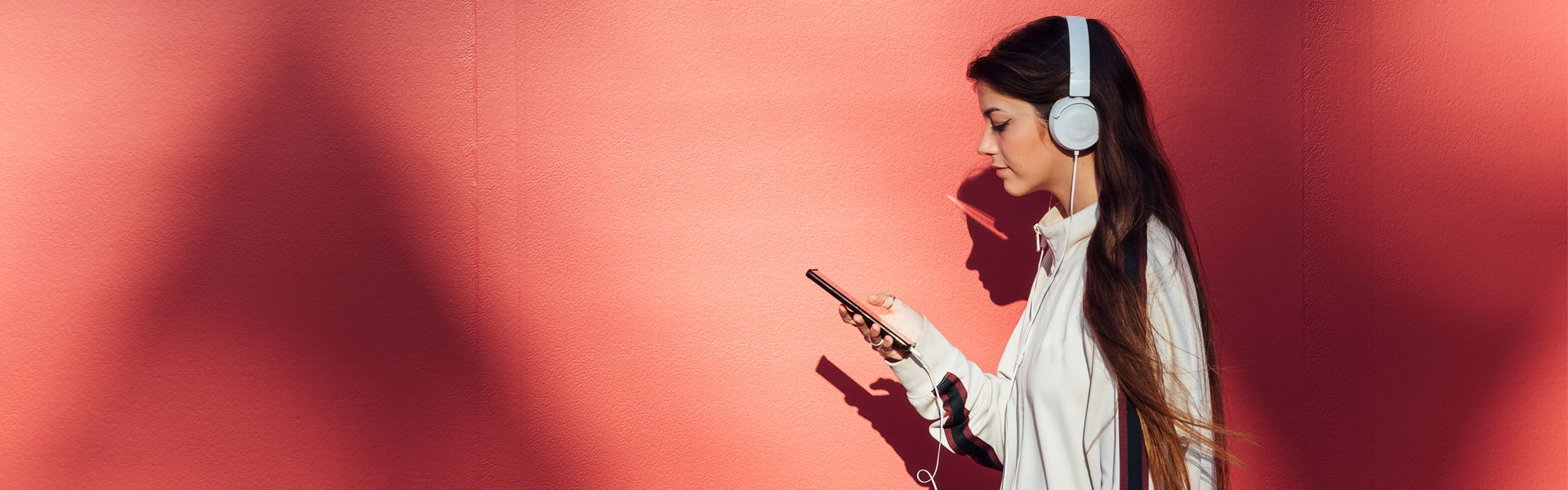 A young woman wearing over-ear headphones listens to music using a mobile device.