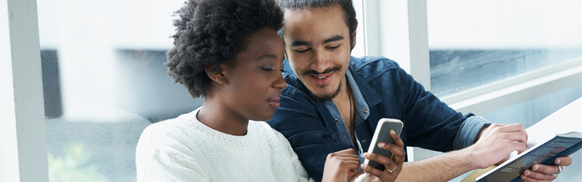 Young man and woman reading from a book and smartphone.