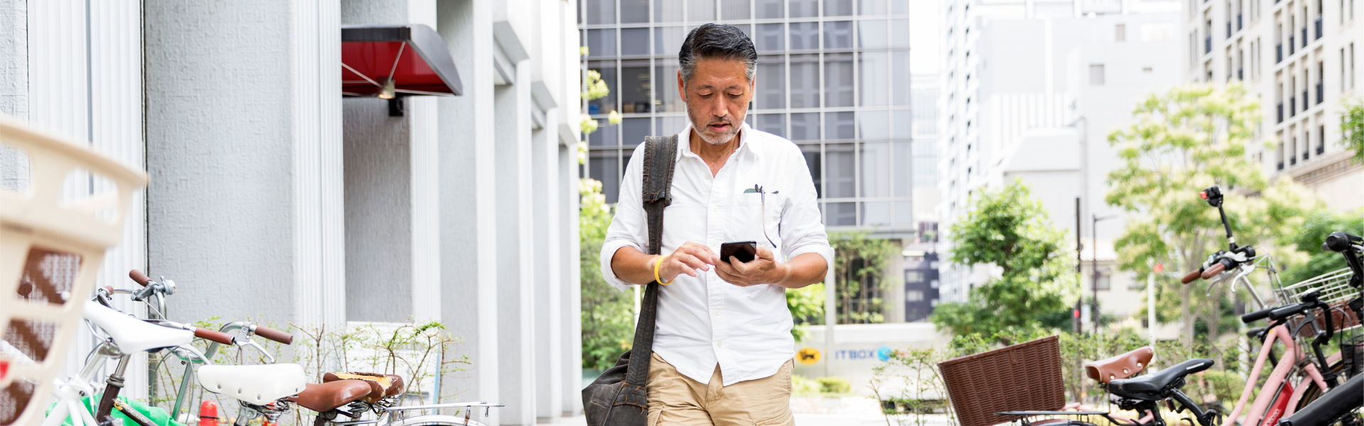 Man in white shirt checks smartphone while walking down a city street.	