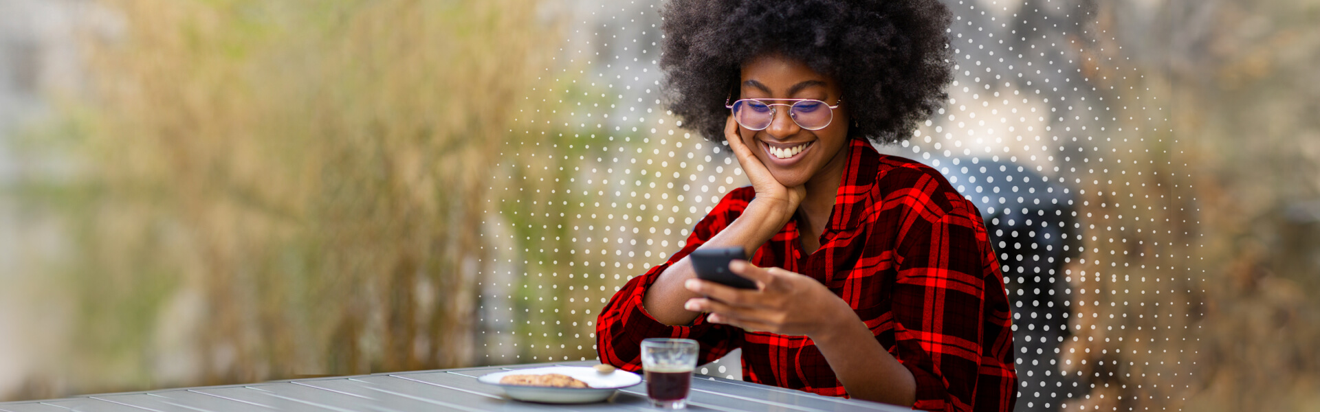A young woman sitting at an outdoor table looks pleased by something she just took care of doing, using her smart phone.