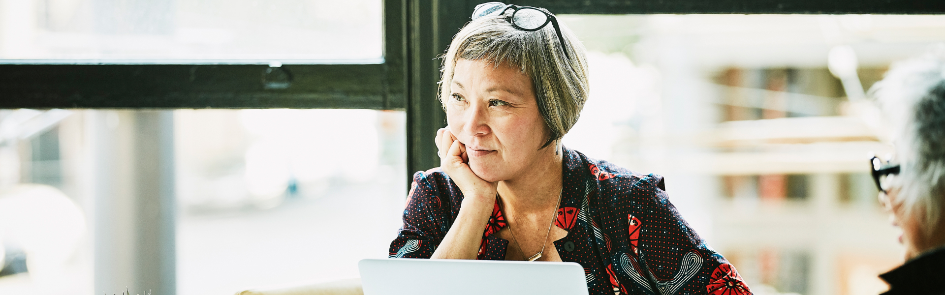 An older woman is sitting in front of a laptop and looking at someone out of the frame.