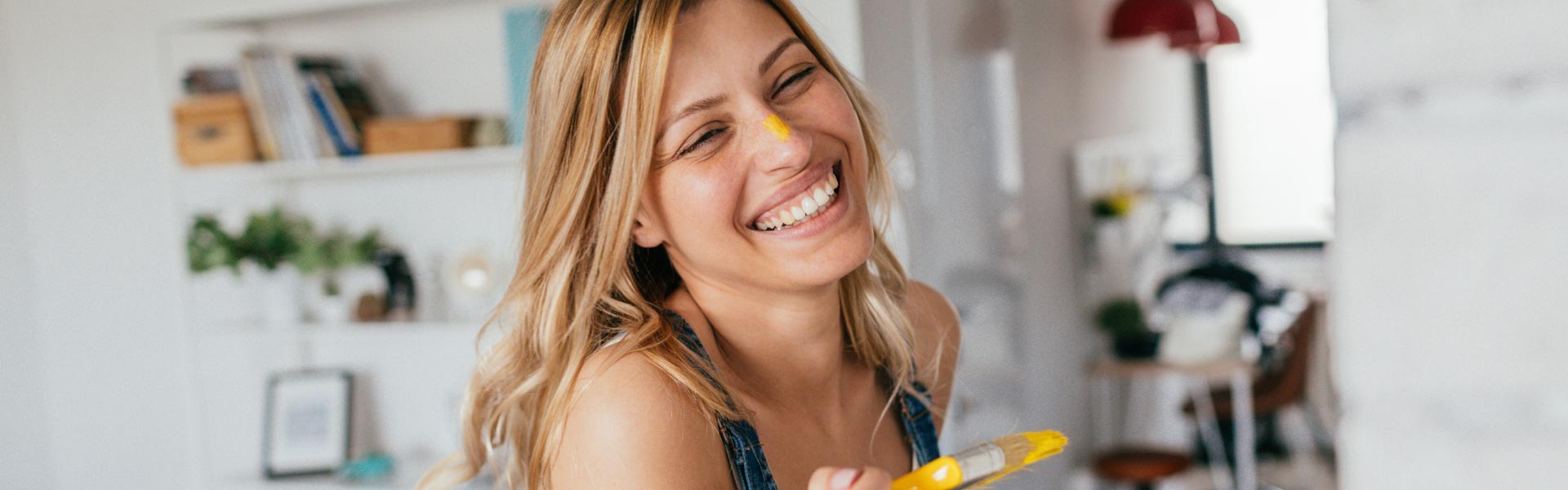 A young woman is smiling while holding a paintbrush.