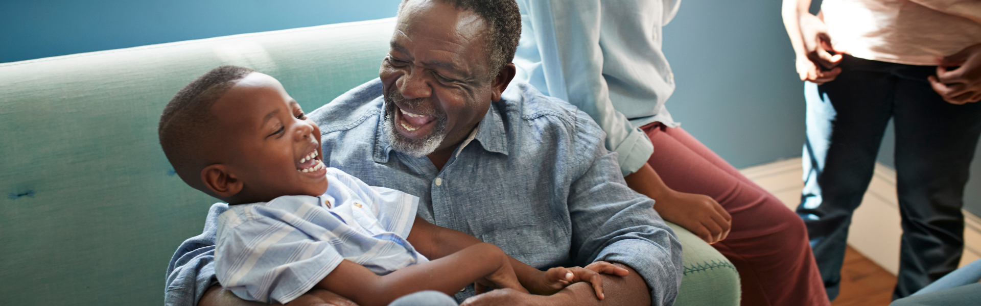 An older man is laughing while cradling a smiling boy in his arms.