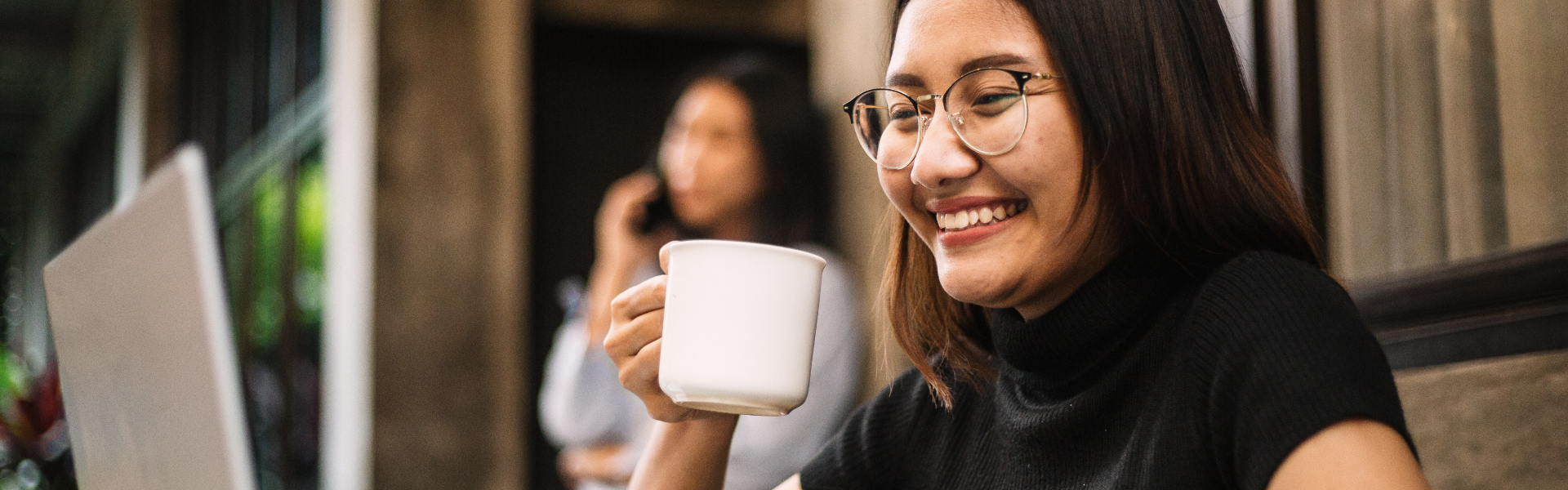 A young, smiling woman is holding up her coffee mug.