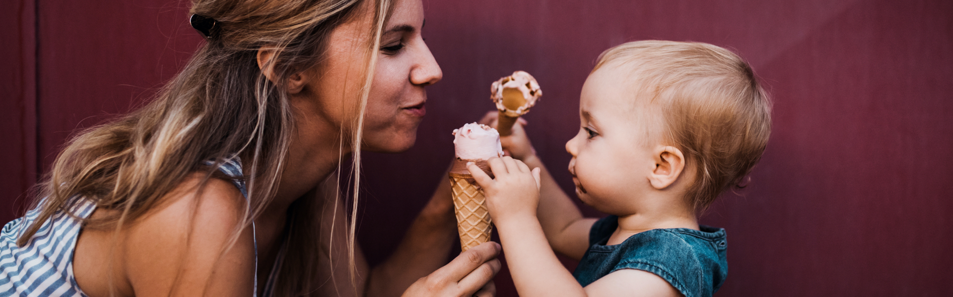 A woman is sharing an ice cream cone with a baby.