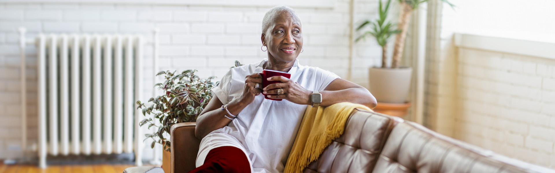 A woman holds a cup of coffee as she reclines on a couch.