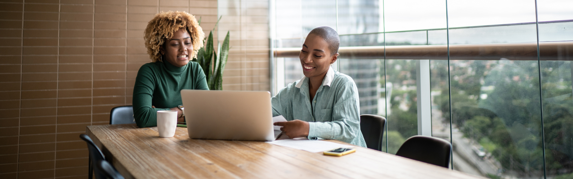 Two young women are working on a shared laptop in an office.