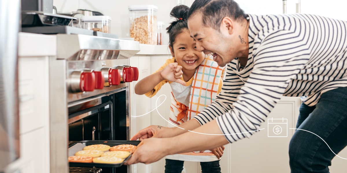 A father takes cookies out of the oven while his daughter looks on with excitement.