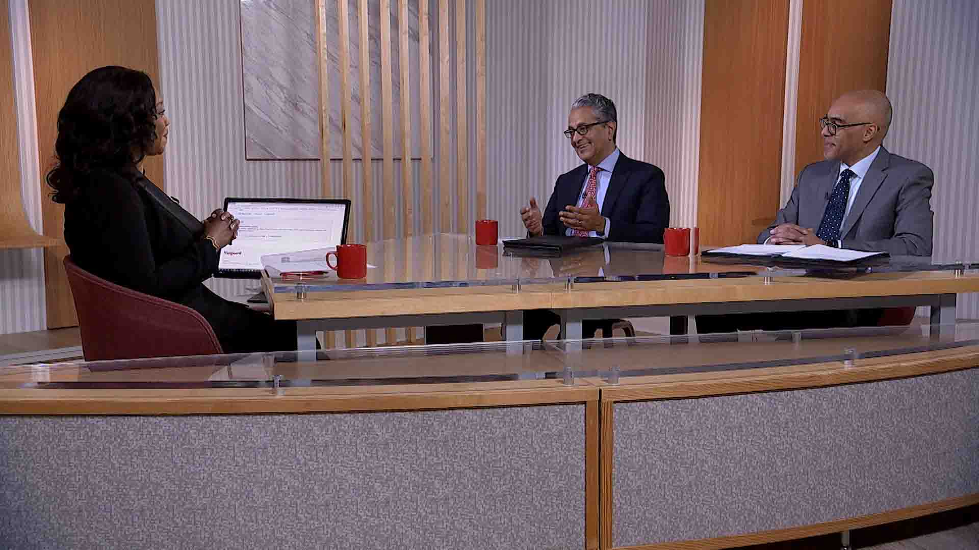 Three executives sit at a desk having a conversation.