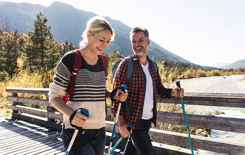 A man and woman are hiking together across a bridge over a running stream.