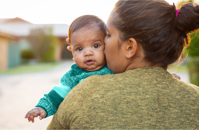 A woman holding a baby is kissing the child on the cheek.