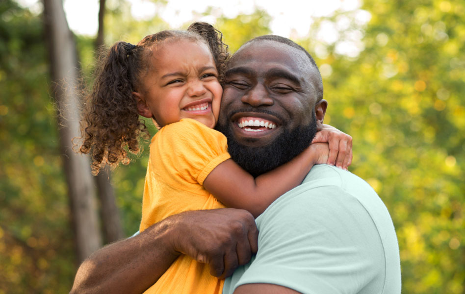 A young, smiling father is embracing his smiling daughter into a tight hug.