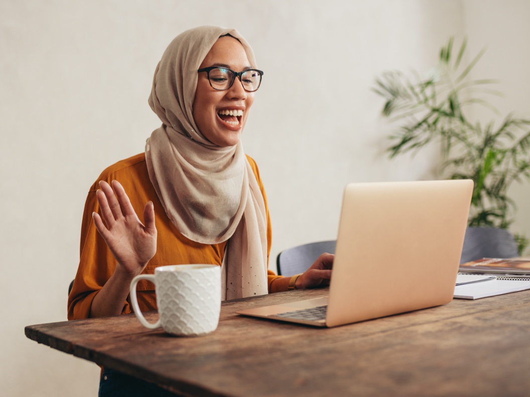 A young woman is happily smiling during a video conference on her laptop.