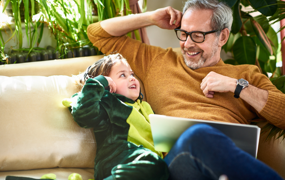 Man on a couch laughing with his costumed grandchild.
