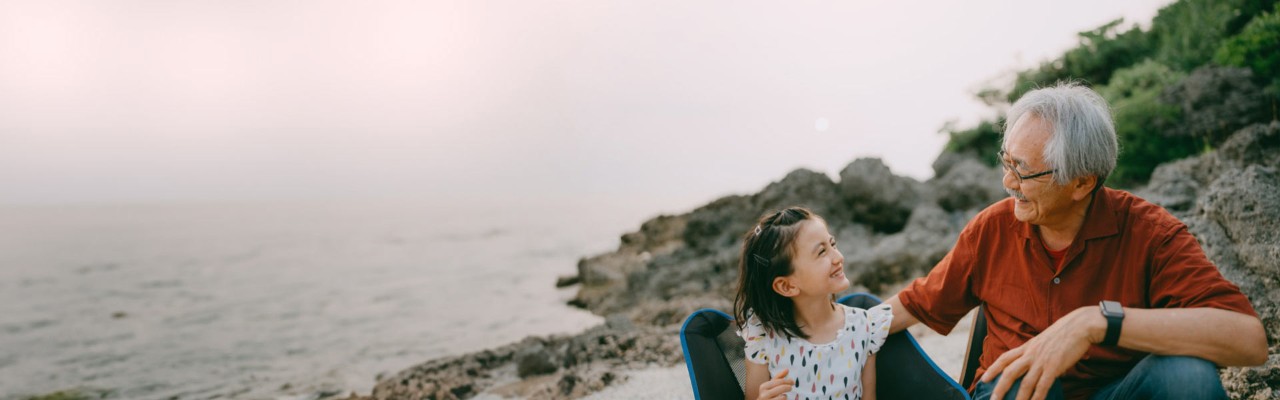 Grandfather and granddaughter sitting on the beach smiling