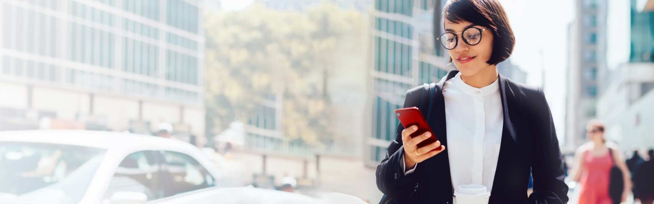 A woman wearing a blazer checks her phone as she walks down a city street.
