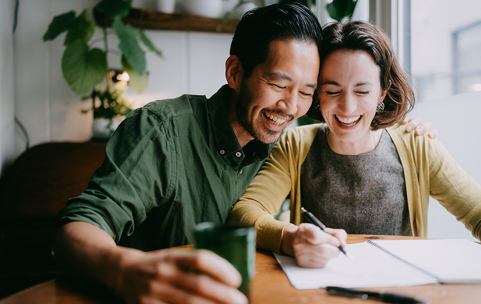 A young couple is smiling and taking notes at a desk.
