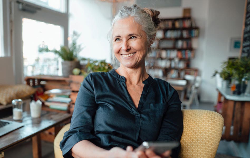 An older woman is holding a smartphone while smiling at someone out of view.
