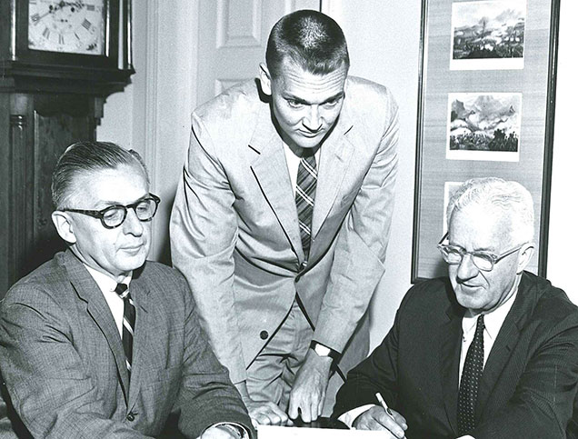 A black and white photo of Jack Bogle working with two colleagues.
