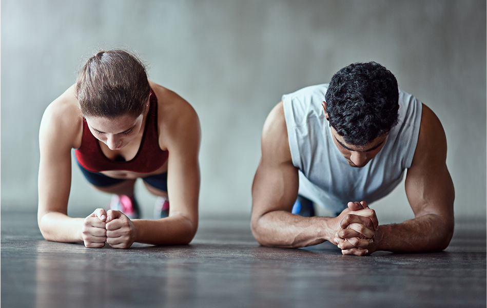 Man and woman planking and looking down in a gym setting.
