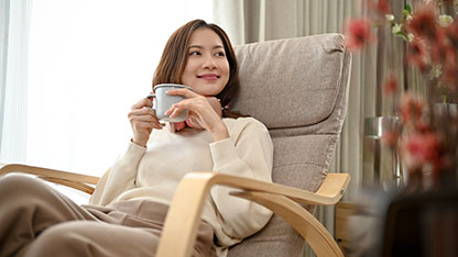 A woman sitting in a chair holds a mug and smiles.