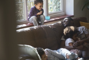 A child is smiling down at her father on a couch.
