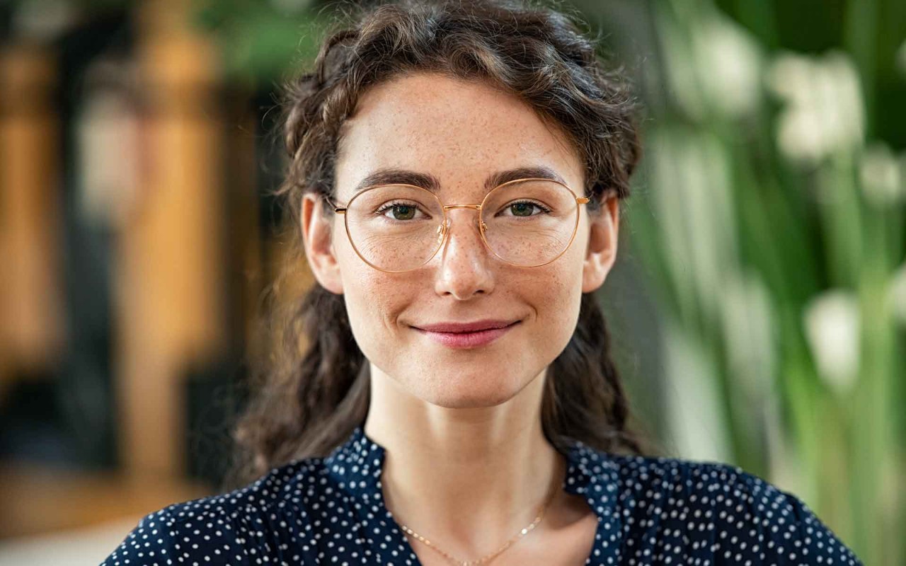 A young woman wearing glasses is confidently smiling directly into the camera.