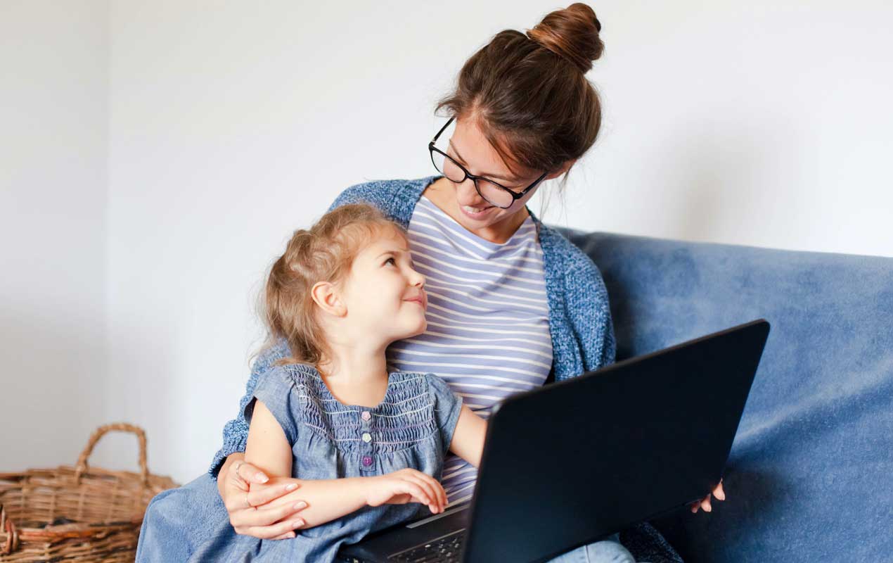A woman is sitting on the couch with a little girl on her lap and a laptop.