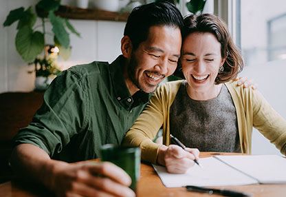 A young couple is smiling and taking notes at a desk.