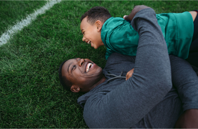 Father and son having fun lying on football field.
