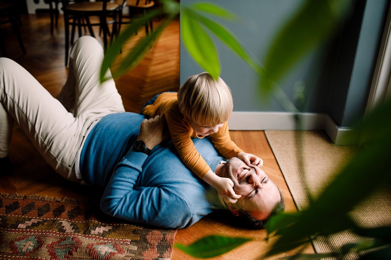 A father is feigning being tackled to the ground by his toddler.