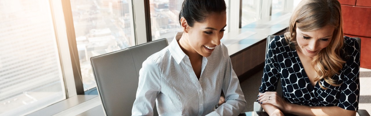 A woman smiling while seated at her desk next to a co-worker.