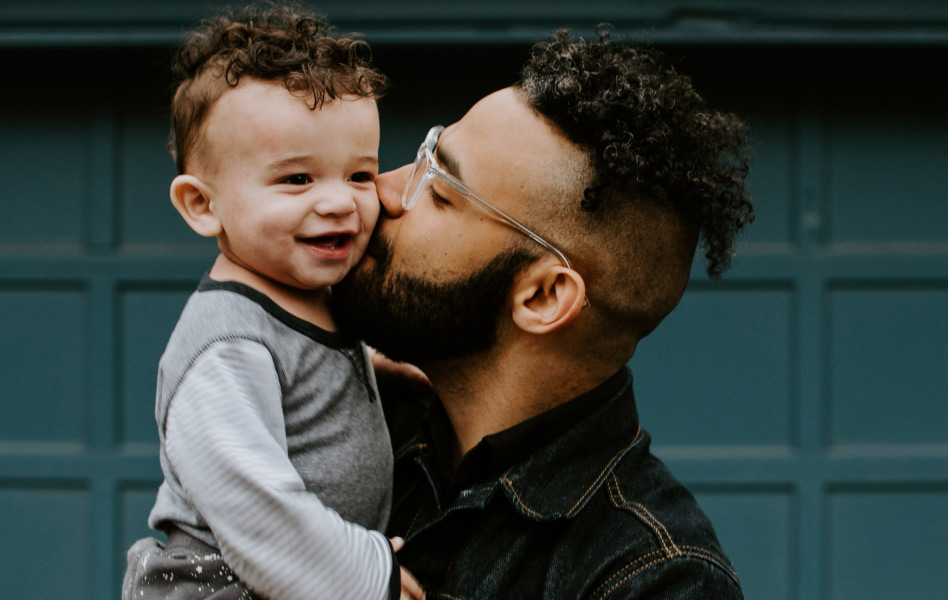 A young father is kissing the cheek of his toddler son.