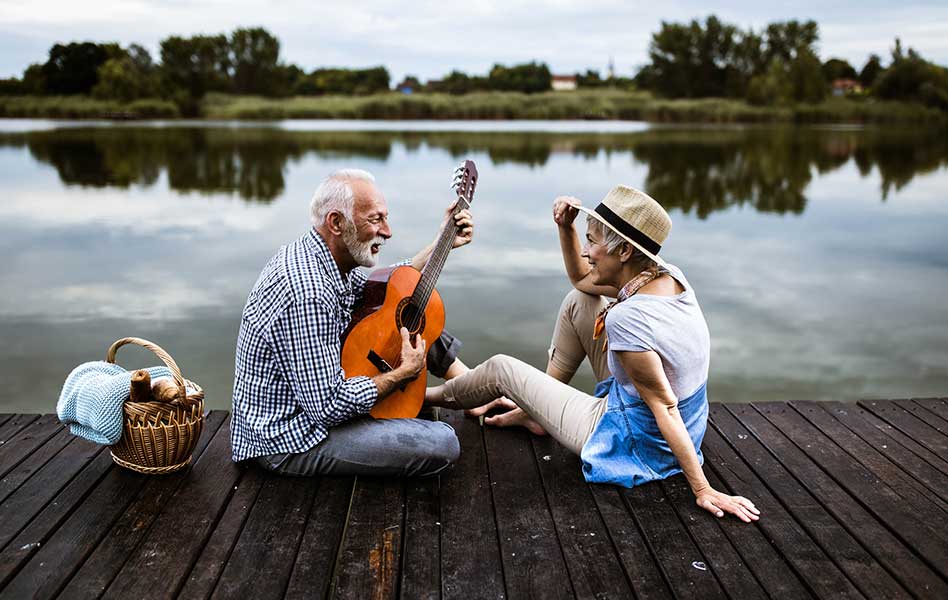 An older man is singing and playing a guitar while facing his smiling wife.