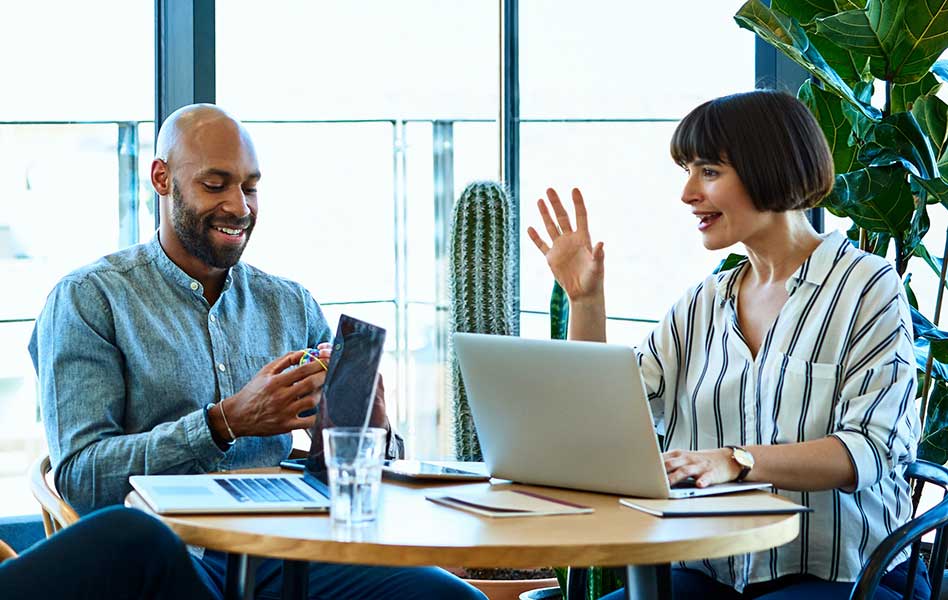 A man, a woman, and another person, seated at a table with laptops, smiling and joyfully discussing retirement plans.