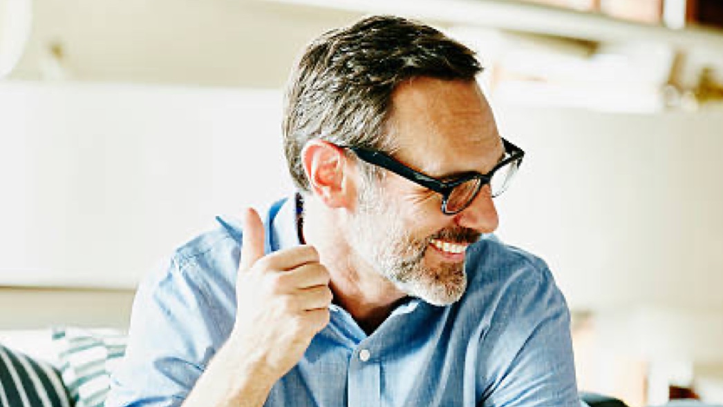 A middle-aged man is smiling off to his left while giving a thumbs up.