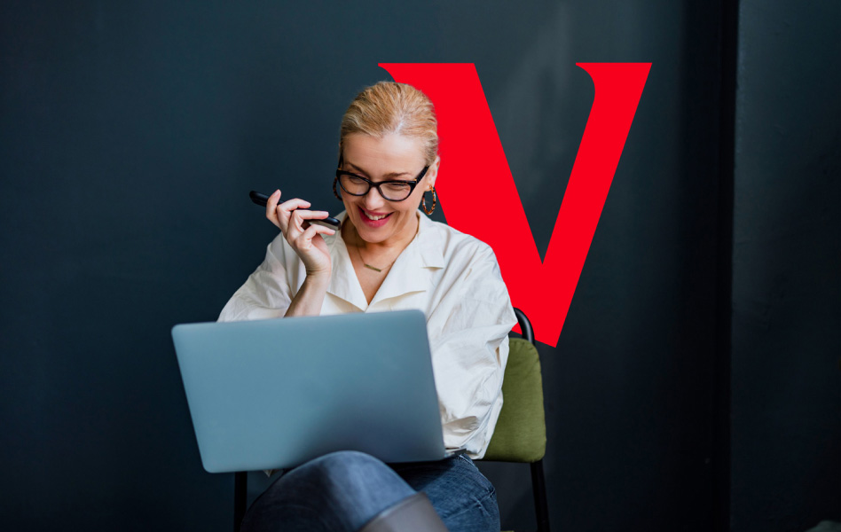 Woman smiling and looking at laptop while on the phone. Vanguard "V" logo is behind her.