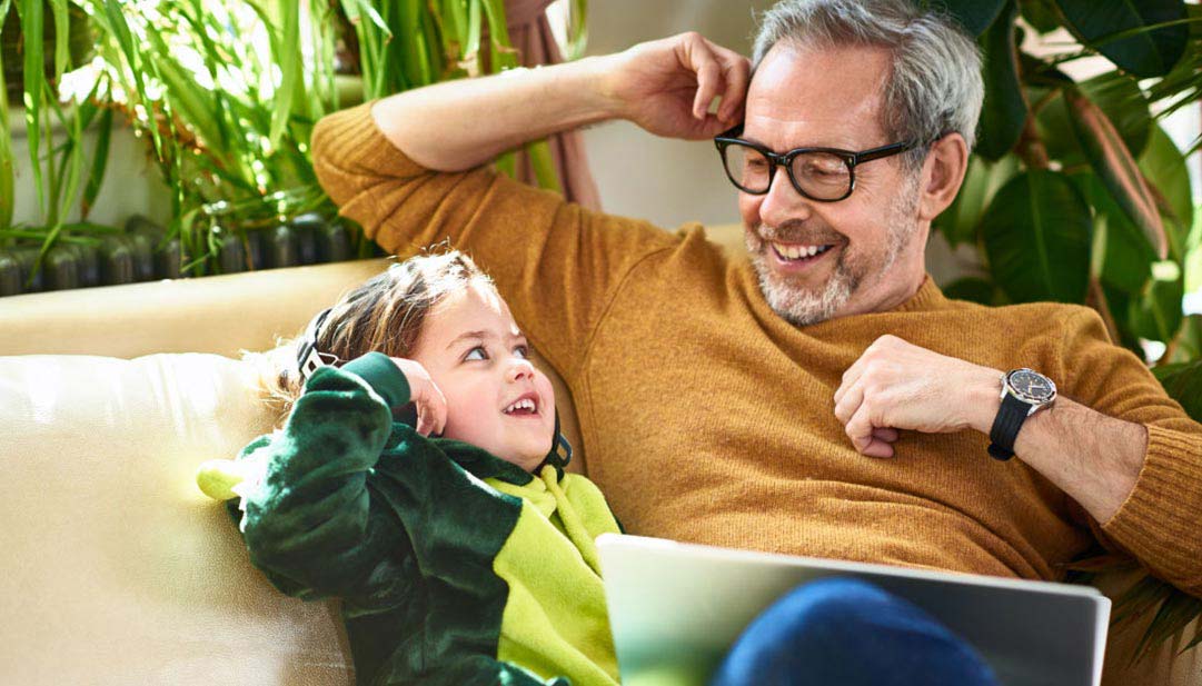 A father and child smile on the couch together. 