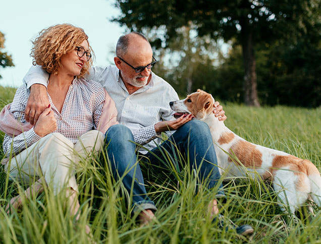 A man and woman are relaxing in a grassy field with their dog at their side.